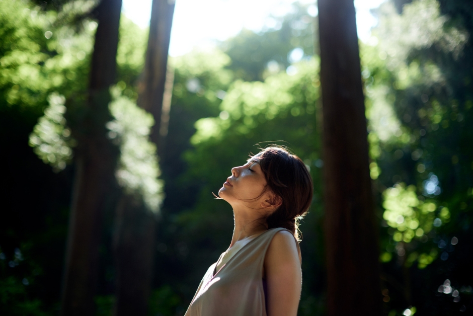 A woman in nature, looking up at the trees