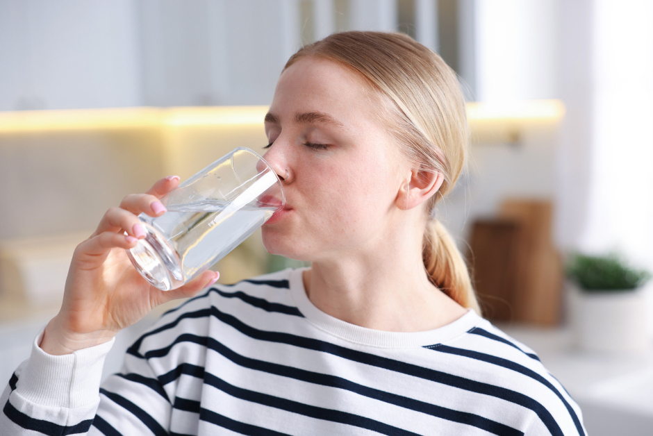 A woman drinking a glass of water in her kitchen