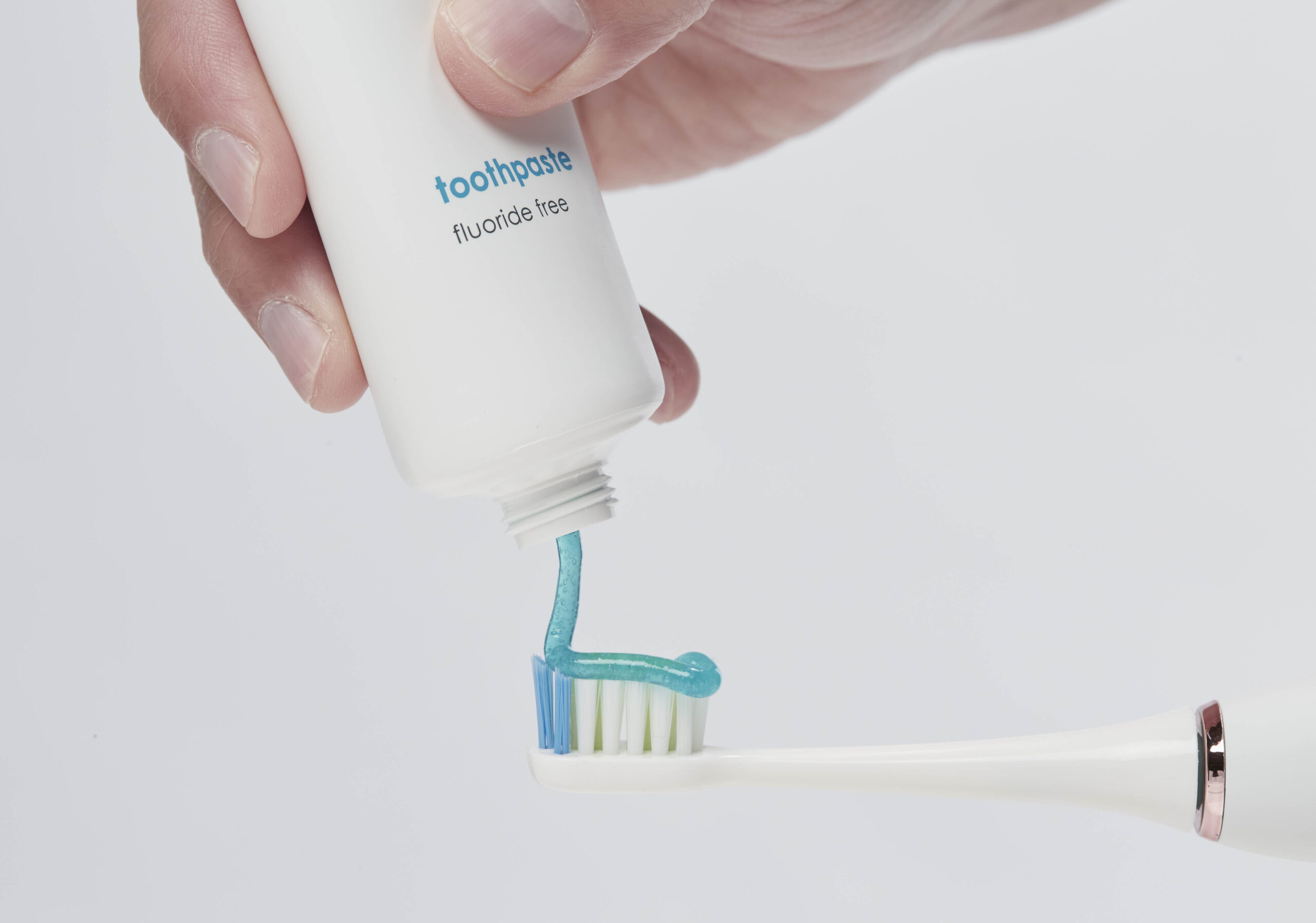 hand squeezing bluem® toothpaste onto a sonic toothbrush