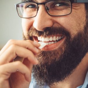 Smiling man with brown beard putting gum in his mouth